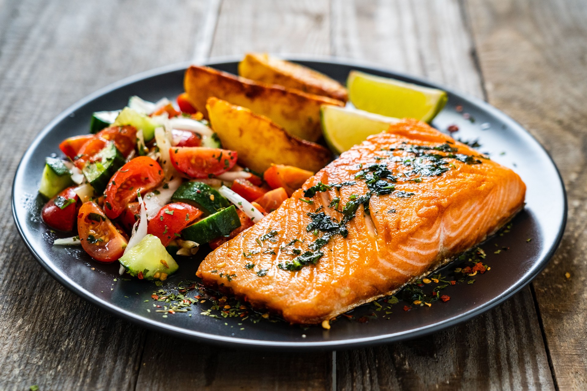 Fried salmon steaks, fried potatoes and fresh vegetables on wooden table